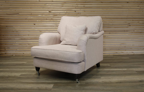 Light pink armchair with a pillow against a wooden paneled wall.