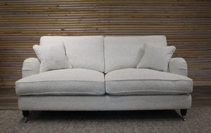 White boucle sofa with cushions against a wooden paneled wall.