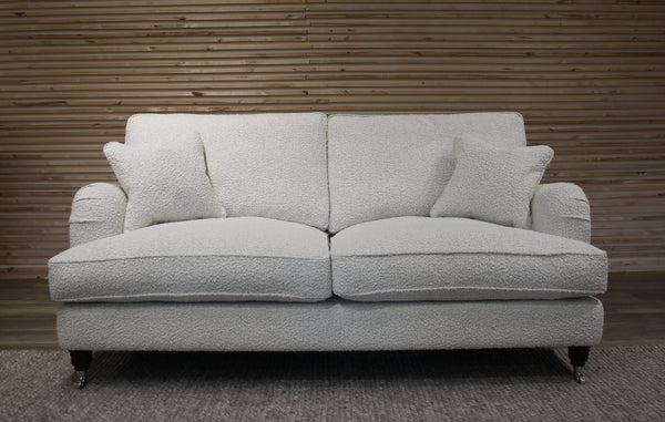 White boucle sofa with cushions against a wooden paneled wall.